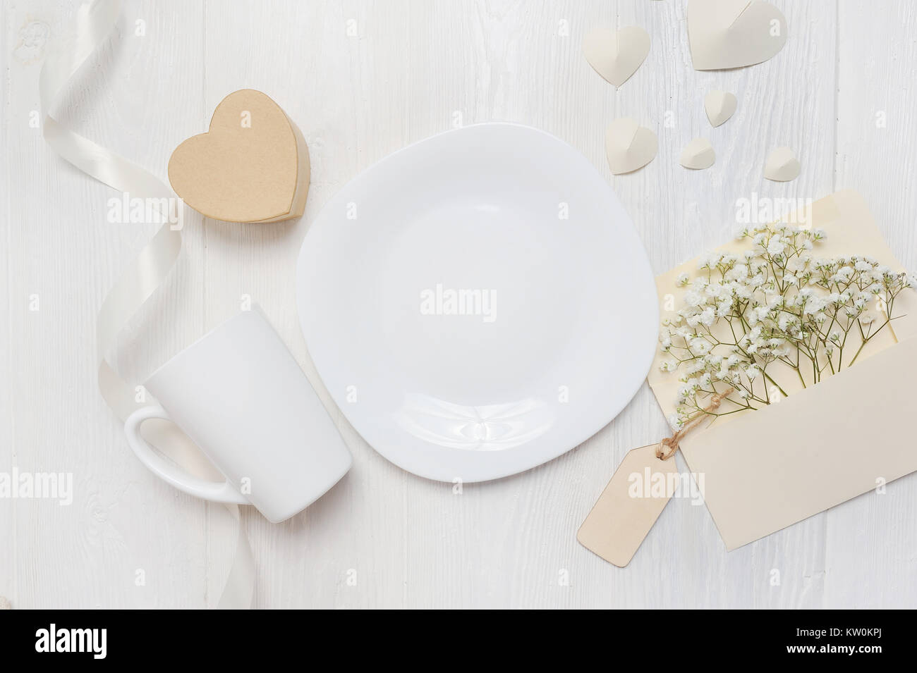 Mockup per il giorno di San Valentino biglietto di auguri lettera nella busta e mug, piastra con Scatola cuore gif, flatlay su un bianco sullo sfondo di legno, con posto fo Foto Stock