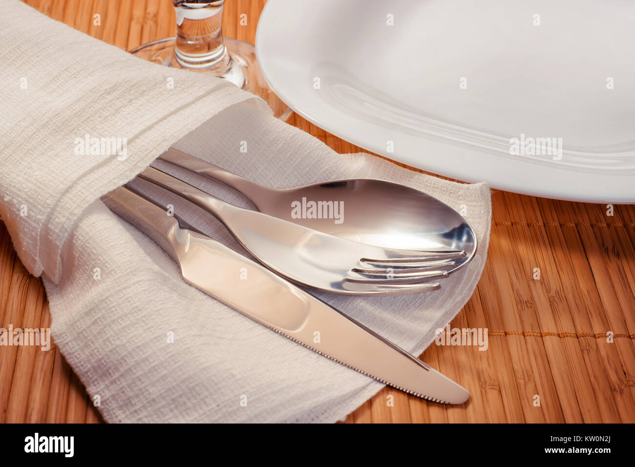 Tabella formale impostazione sul tappetino di bambù. Piastra bianca, posate e vetro. Vista laterale, dai toni caldi immagine Foto Stock