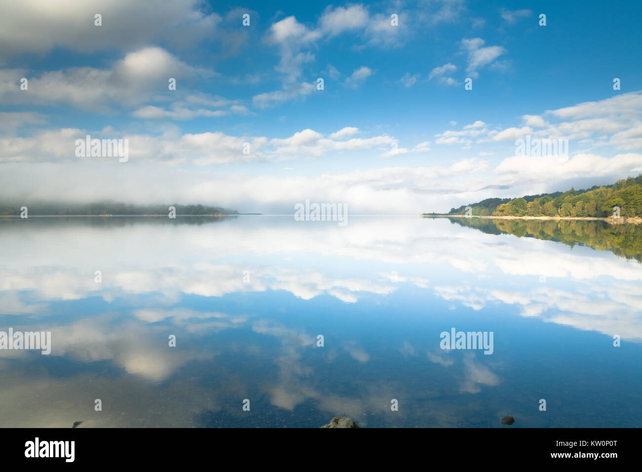 I colori autunnali, il cielo blu e nuvole bianche riflettere serenamente su uno specchio liscia e continua a Loch Katrine, Perthshire Scozia Scotland Foto Stock