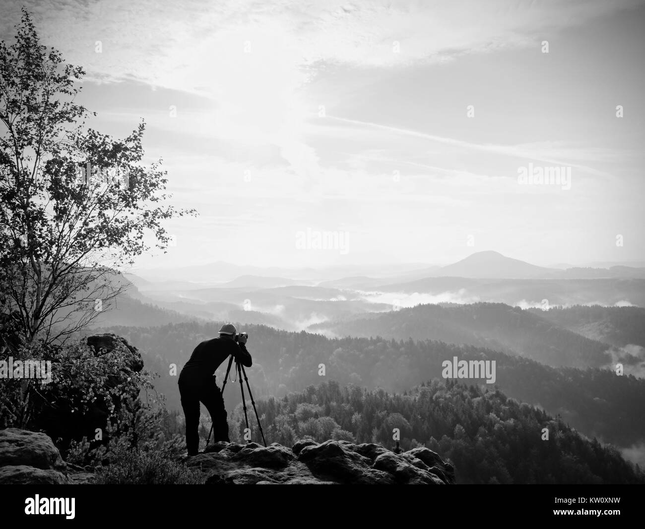 Fotografo di natura soggiorno al treppiede sul vertice e pensare. Collinare paesaggio di nebbia in primo colori autunnali. Foto Stock