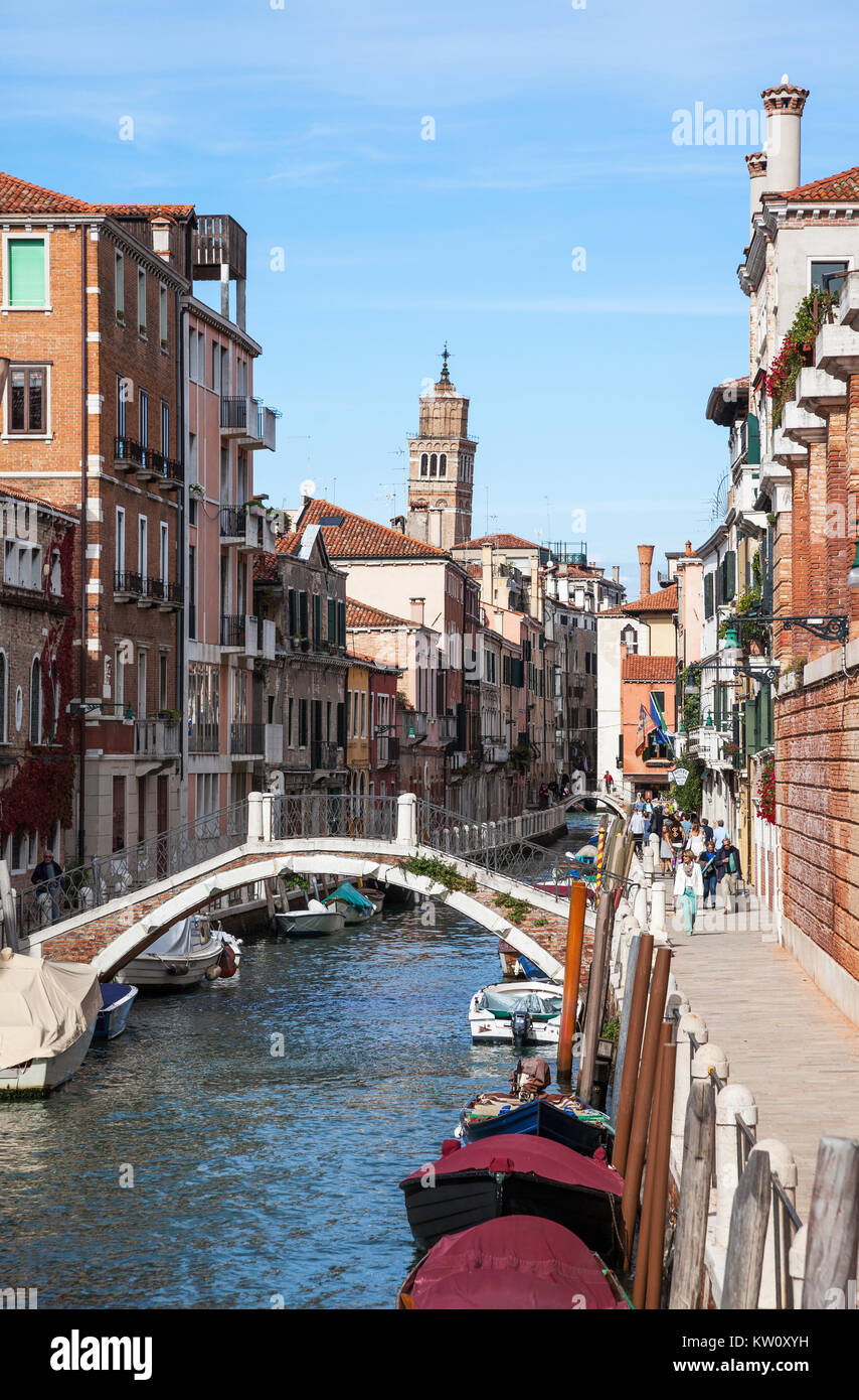 Visualizza in basso Rio de la Fornace Canal a Venezia con tante barche ormeggiate e persone che passeggiano in un giorno caldo e soleggiato Foto Stock