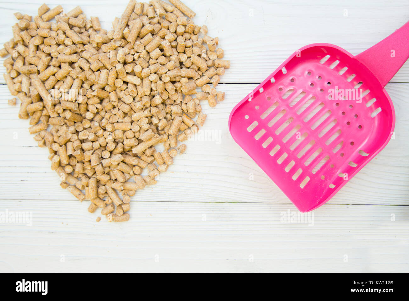 Pet care concetto. Un cuore fatto di pet wc del bocchettone di rifornimento e di un wc rosa scoop. Tappapori per animali domestici- gatti, topi, ratti, conigli, criceti. Legno bianco b Foto Stock