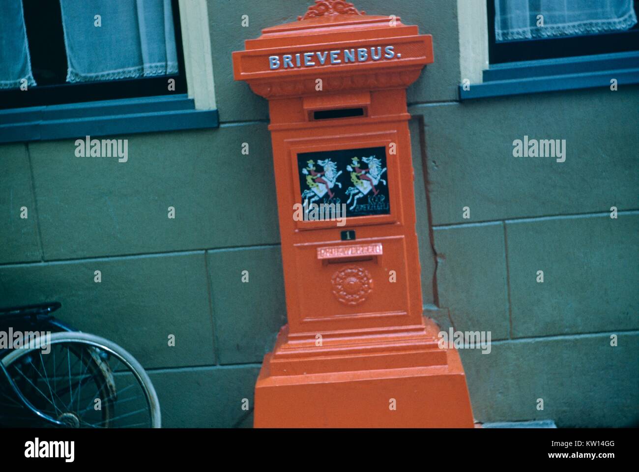 Cassetta postale in rosso con la dicitura 'brievenbus' o 'Mailbox', con una bicicletta appoggiata contro una parete, Olanda, 1952. Foto Stock