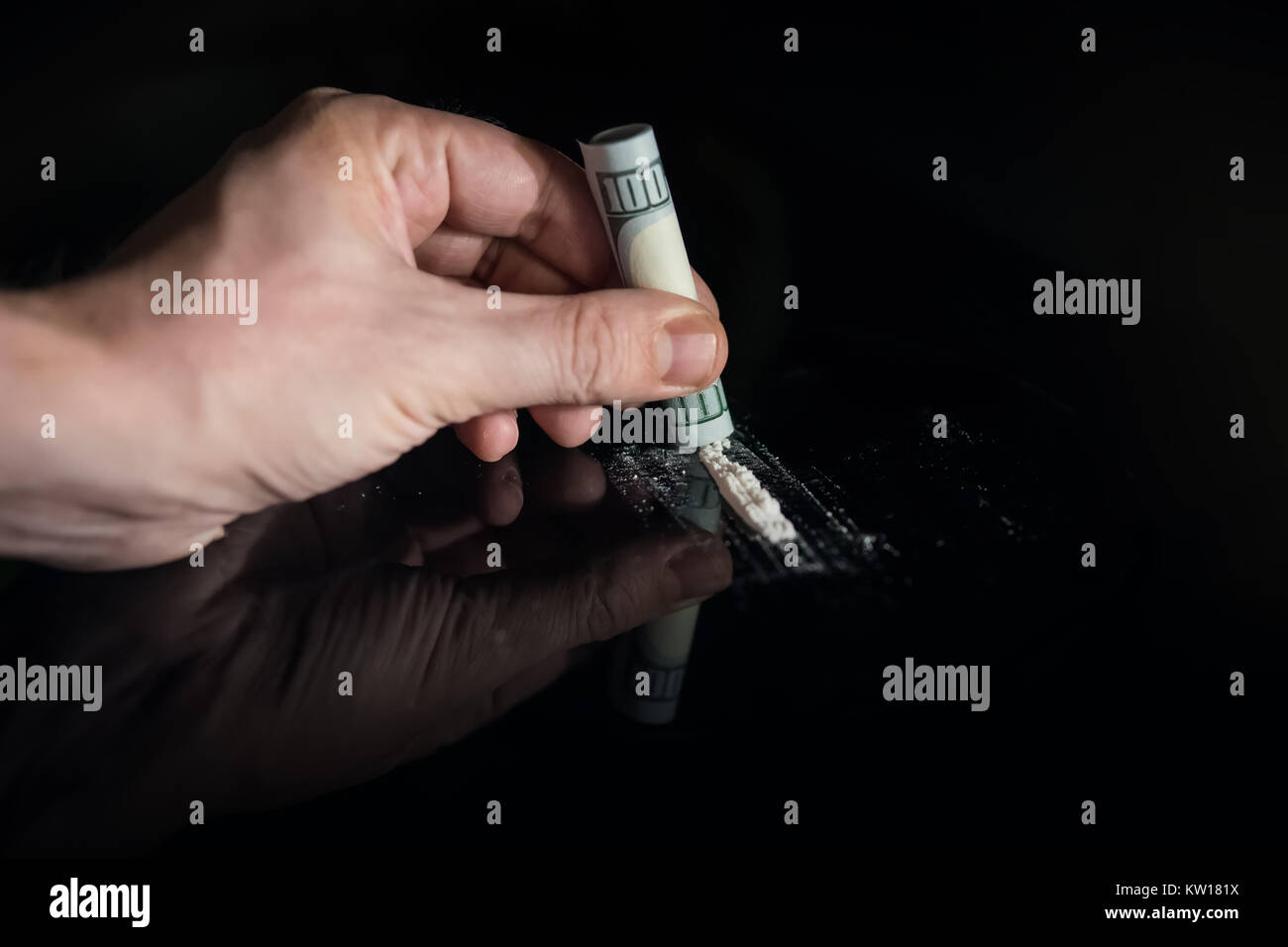 Man mano rotoli dollar banconota per l'uso di cocaina in polvere linee, la tossicodipendenza concetto. Una linea di coke con un centinaio di dollari su sfondo nero. Foto Stock