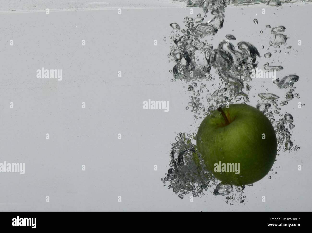 Verde mela caduta in acqua in corrispondenza di un angolo, circondato da bolle di aria. Sfondo grigio chiaro Foto Stock