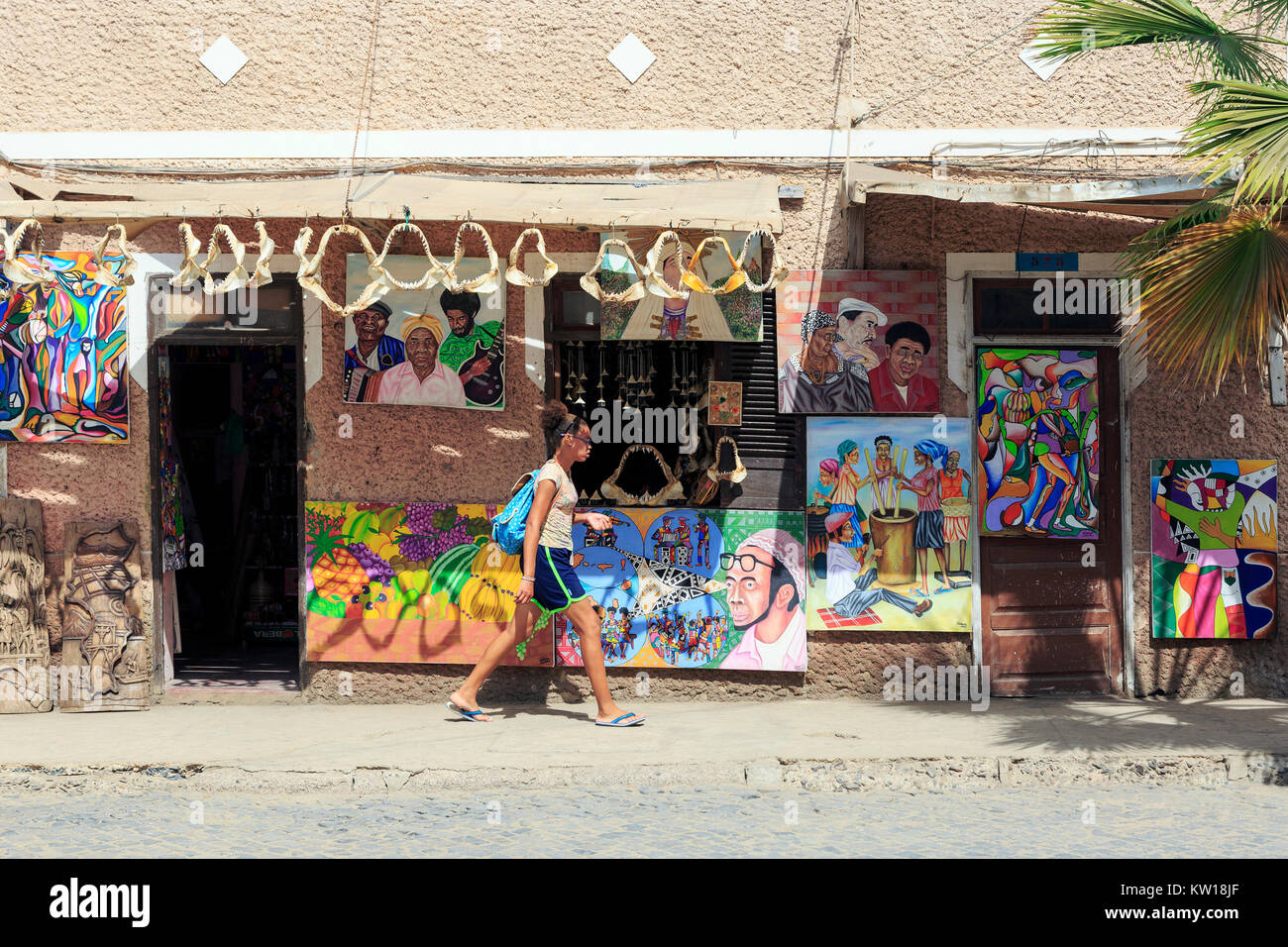 Giovane ragazza locale oltrepassando un souvenir turistici negozio di vendita di opere d'arte e gli squali ganasce, Santa Maria, Sal, Salina, Capo Verde, Africa Foto Stock