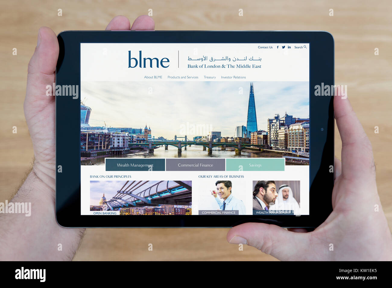 Un uomo guarda presso la banca di Londra e il Medio Oriente (BLME) Sito web sul suo iPad dispositivo tablet pc, su un tavolo di legno top sfondo (solo uso editoriale) Foto Stock