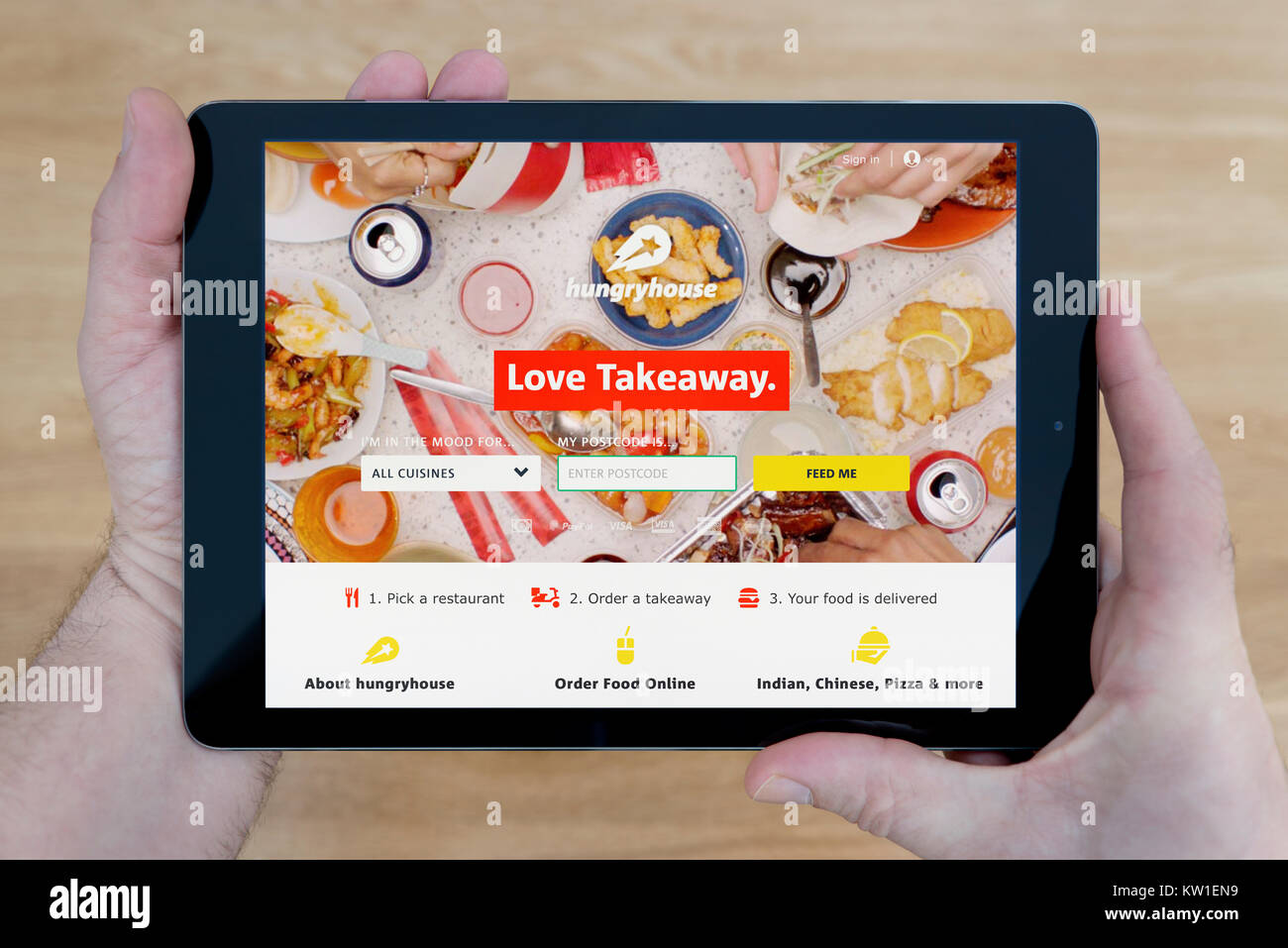 Un uomo guarda la fame House sito web sul suo iPad dispositivo tablet, sparato contro un tavolo di legno top sfondo (solo uso editoriale) Foto Stock