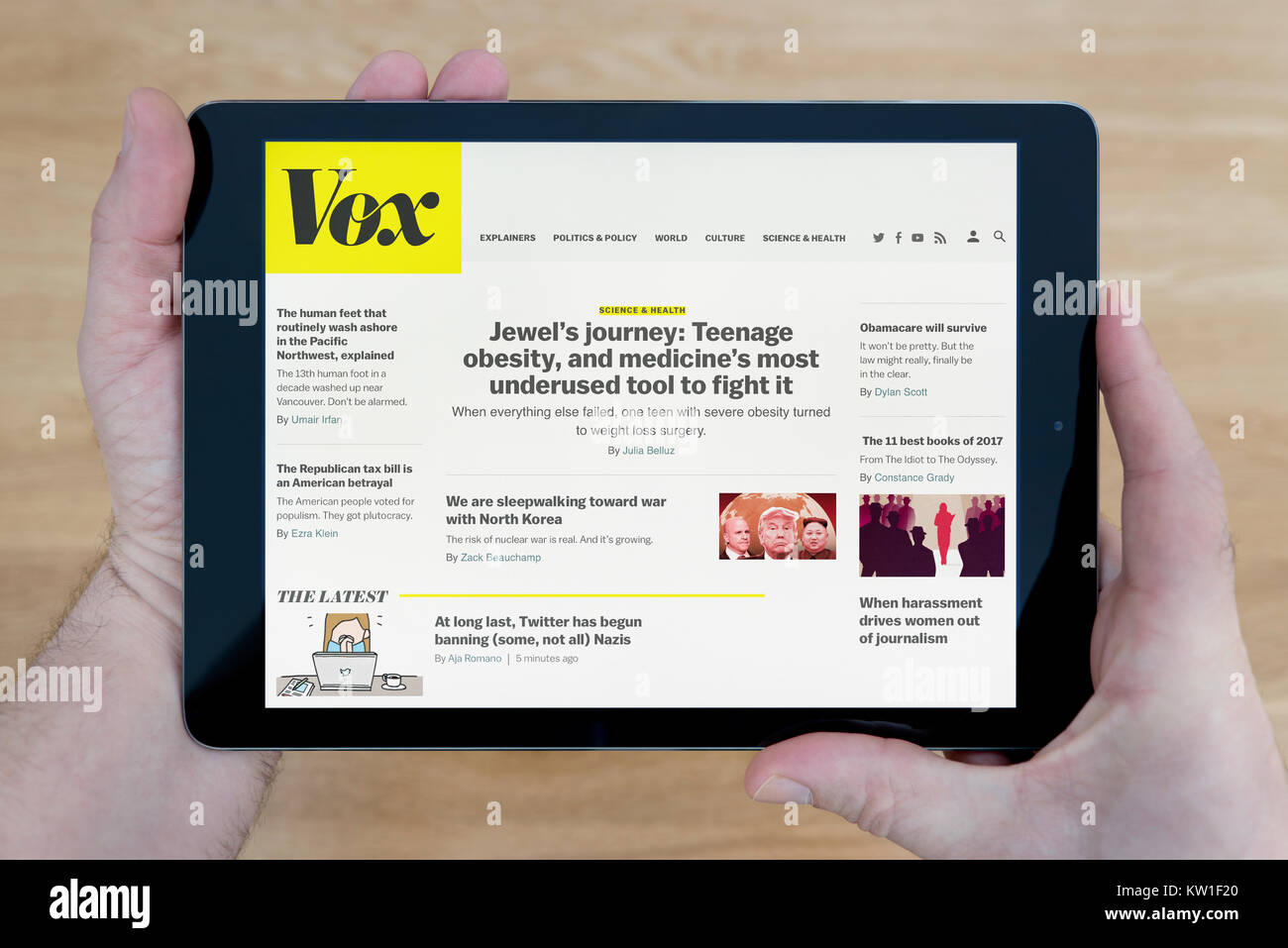 Un uomo guarda il sito web Vox sul suo iPad dispositivo tablet, sparato contro un tavolo di legno top sfondo (solo uso editoriale) Foto Stock