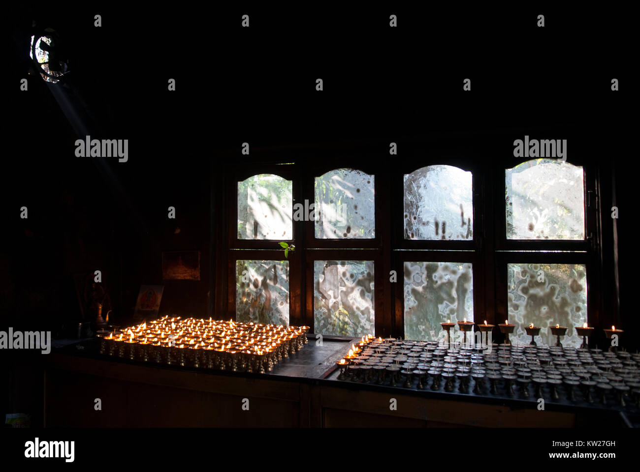 Candela in camera il monastero tibetano: di fronte alla finestra vi è una tabella con lampade a olio burning stoppini sono bruciore, al di fuori della finestra si vede un Foto Stock