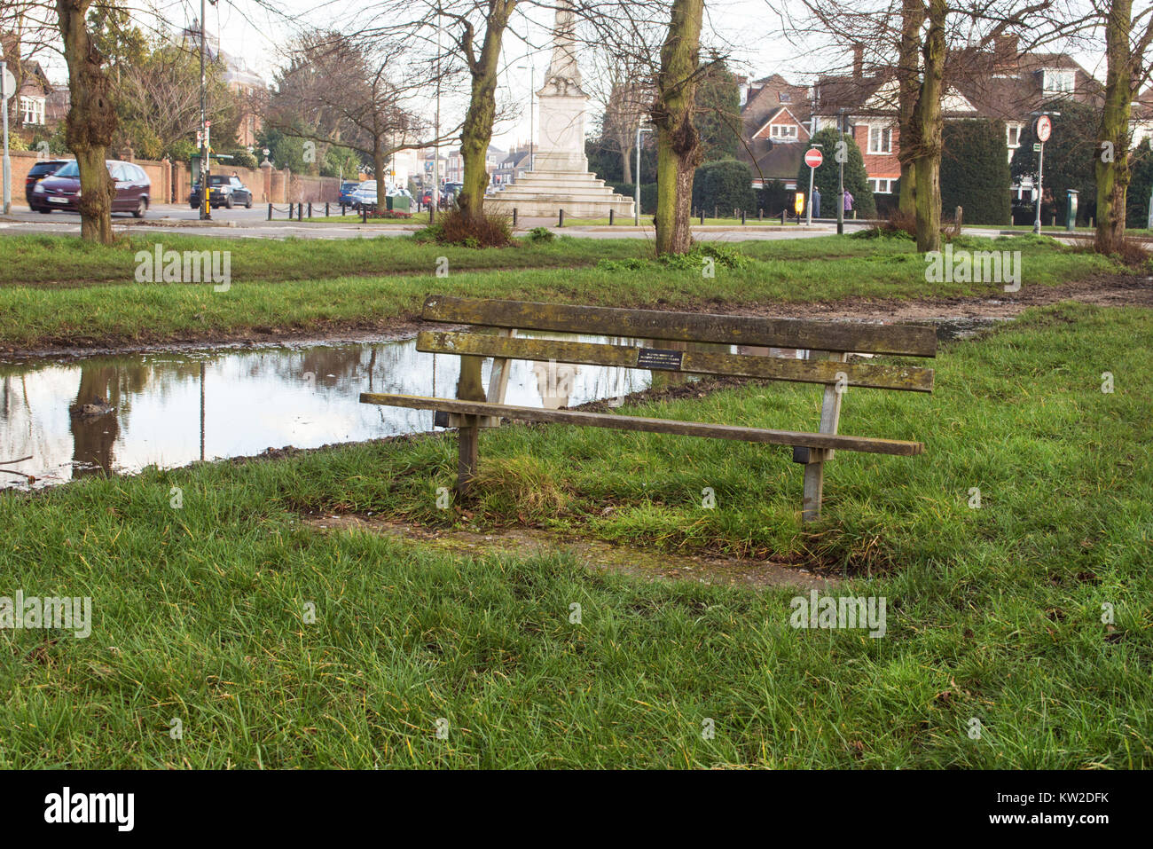 Immagine di panorama di un di legno una panchina nel parco circondato da grande pozza, luminoso verde erba e alberi. Statua in background. Bella e soleggiata giornata d'autunno. Foto Stock