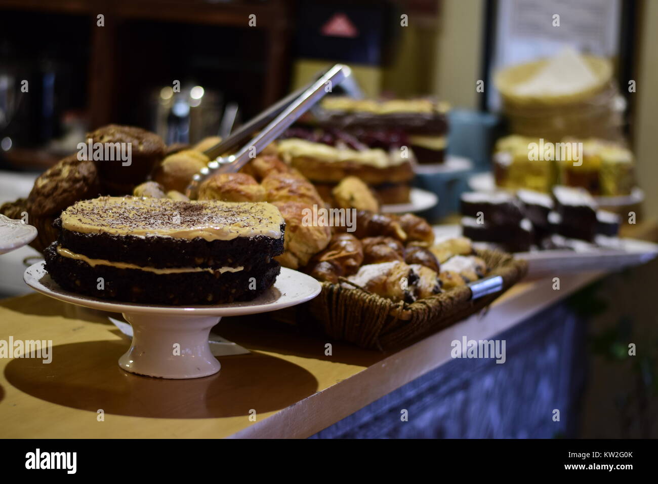Varietà di beni cotti al forno su un contatore in un negozio di dolci con un cioccolato a strati di pan di spagna in primo piano Foto Stock