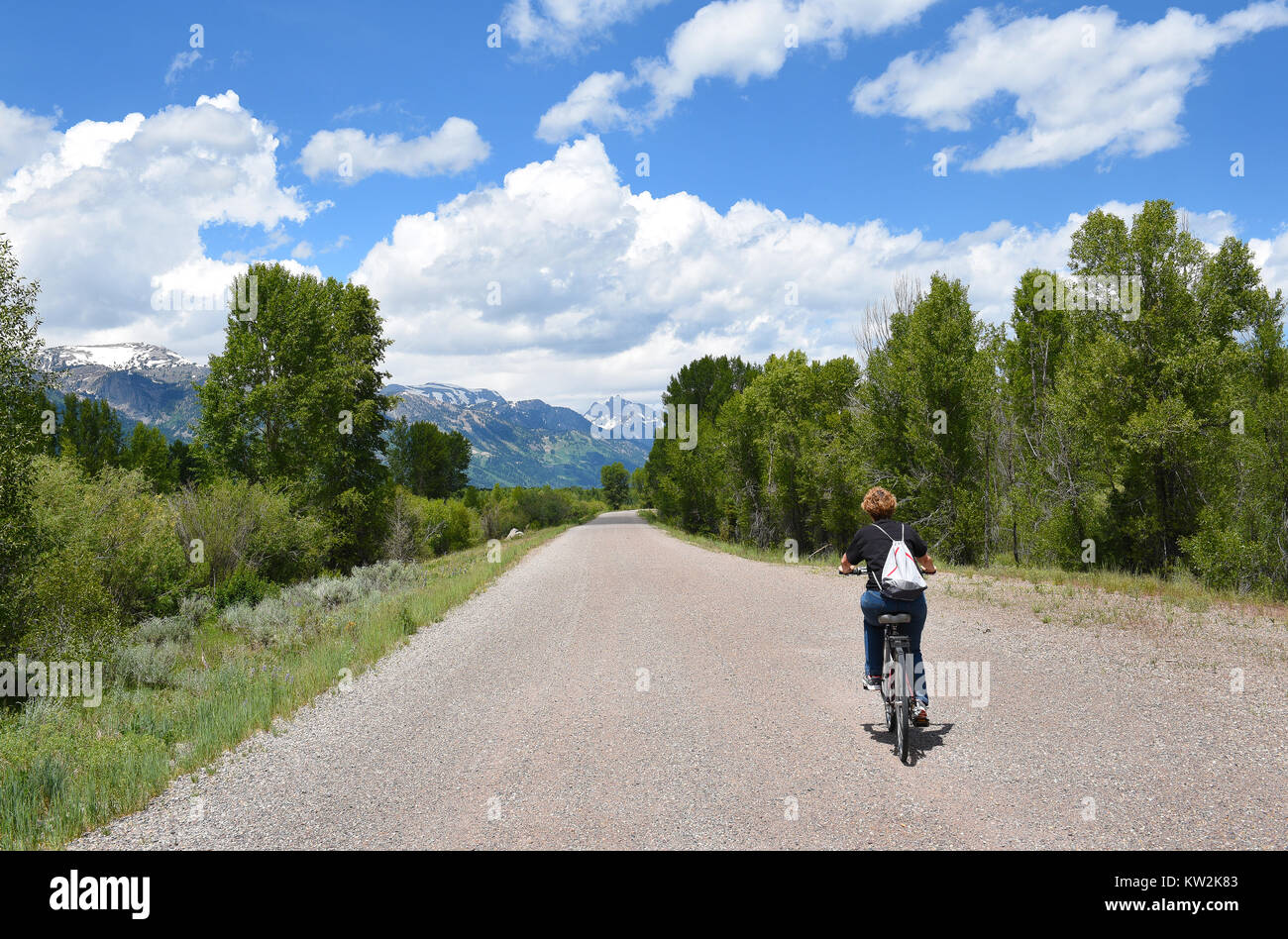 Donna in bicicletta lungo una pista ciclabile in Jackson Hole, Wyoming. Il Grand Tetons sono in distanza. Foto Stock