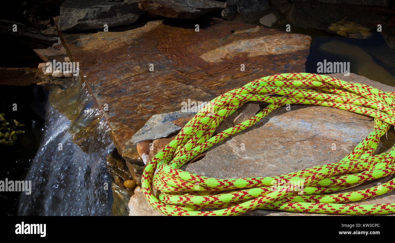 Giallo arrampicata corda avvolta su una roccia accanto a un flusso Foto Stock