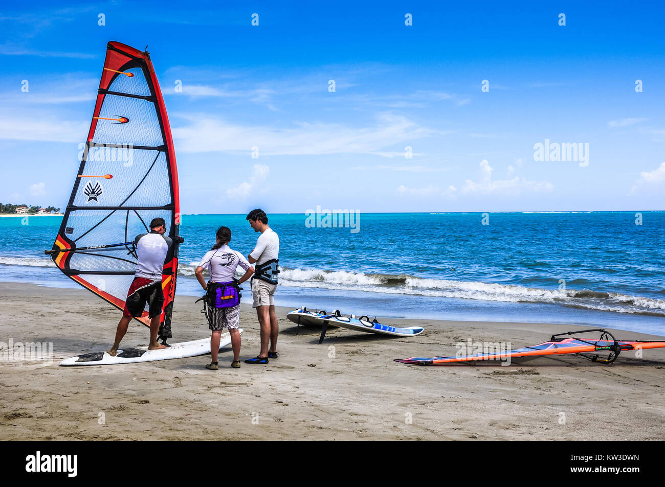 Una giovane coppia attiva tiene una lezione di windsurf con un istruttore sulla sabbia al ocean shore in Cabarete Repubblica Dominicana. Foto Stock
