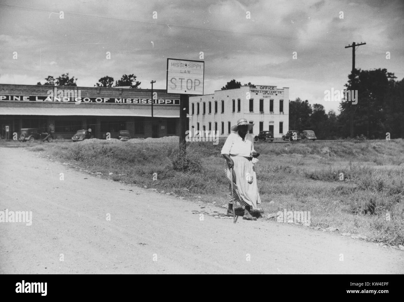 Una donna cammina lungo una strada sterrata nei pressi di negozi, uffici, e clinica su una piantagione di cotone del Delta Società di pino di Scott, Mississippi, ottobre 1939. Foto Stock