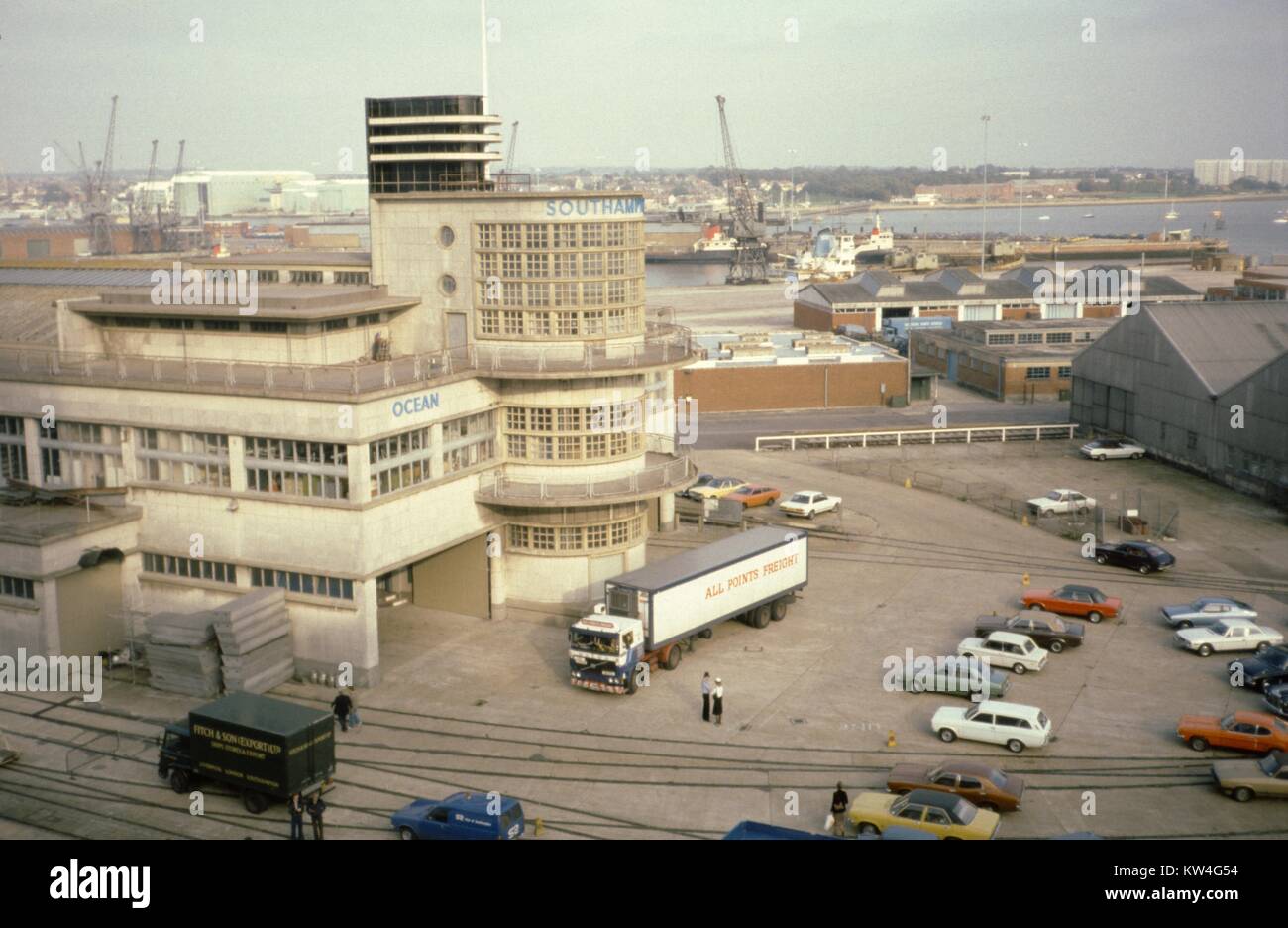 Porto di Southampton, con camion di consegna, gru, magazzini di stoccaggio e di un piccolo parcheggio con vetture visibili, Southampton, Regno Unito, 1975. Foto Stock