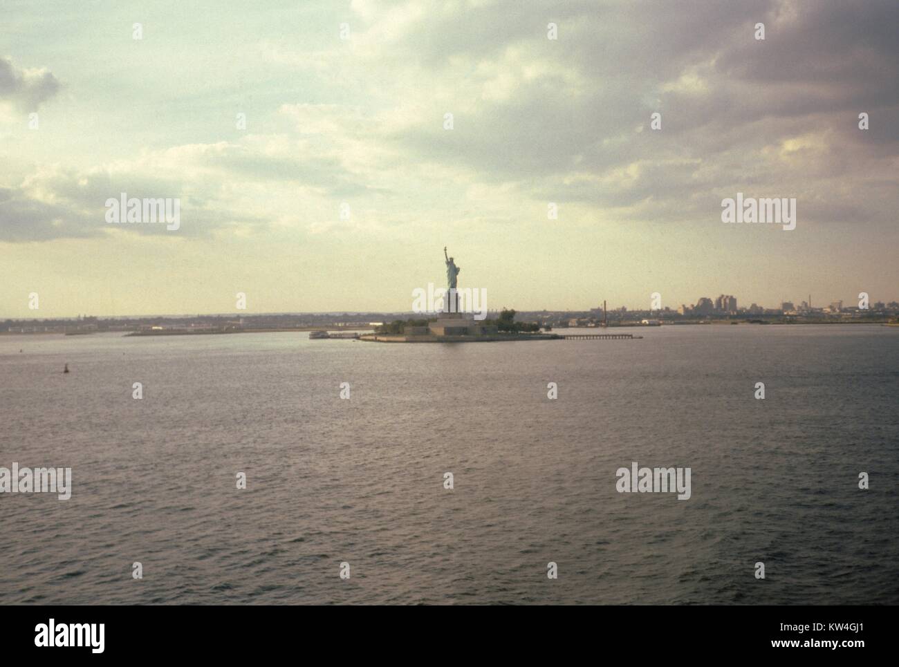 Statua della Libertà visto da una distanza al tramonto sotto le nuvole di raccolta da una nave nel porto di New York, New York, New York, 1975. Foto Stock