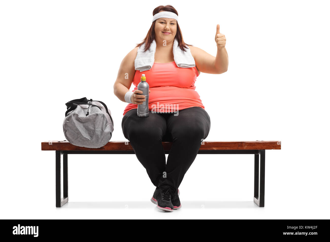 Il sovrappeso donna seduta su una panchina di legno accanto a una borsa sportiva rendendo un pollice in alto segno isolato su sfondo bianco Foto Stock
