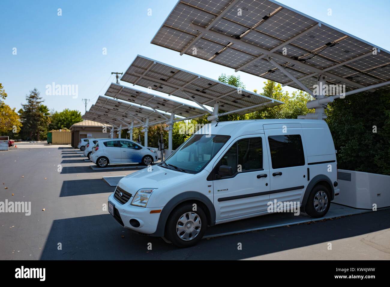 Al Googleplex, sede del motore di ricerca Google società nella Silicon Valley Town di Mountain View, California, un piccolo furgone elettrico è parcheggiato all'ombra di un array solare che alimenta una stazione di ricarica per il van, con altre stazioni di ricarica e i veicoli elettrici visibili in background, Mountain View, California, 24 agosto 2016. Foto Stock