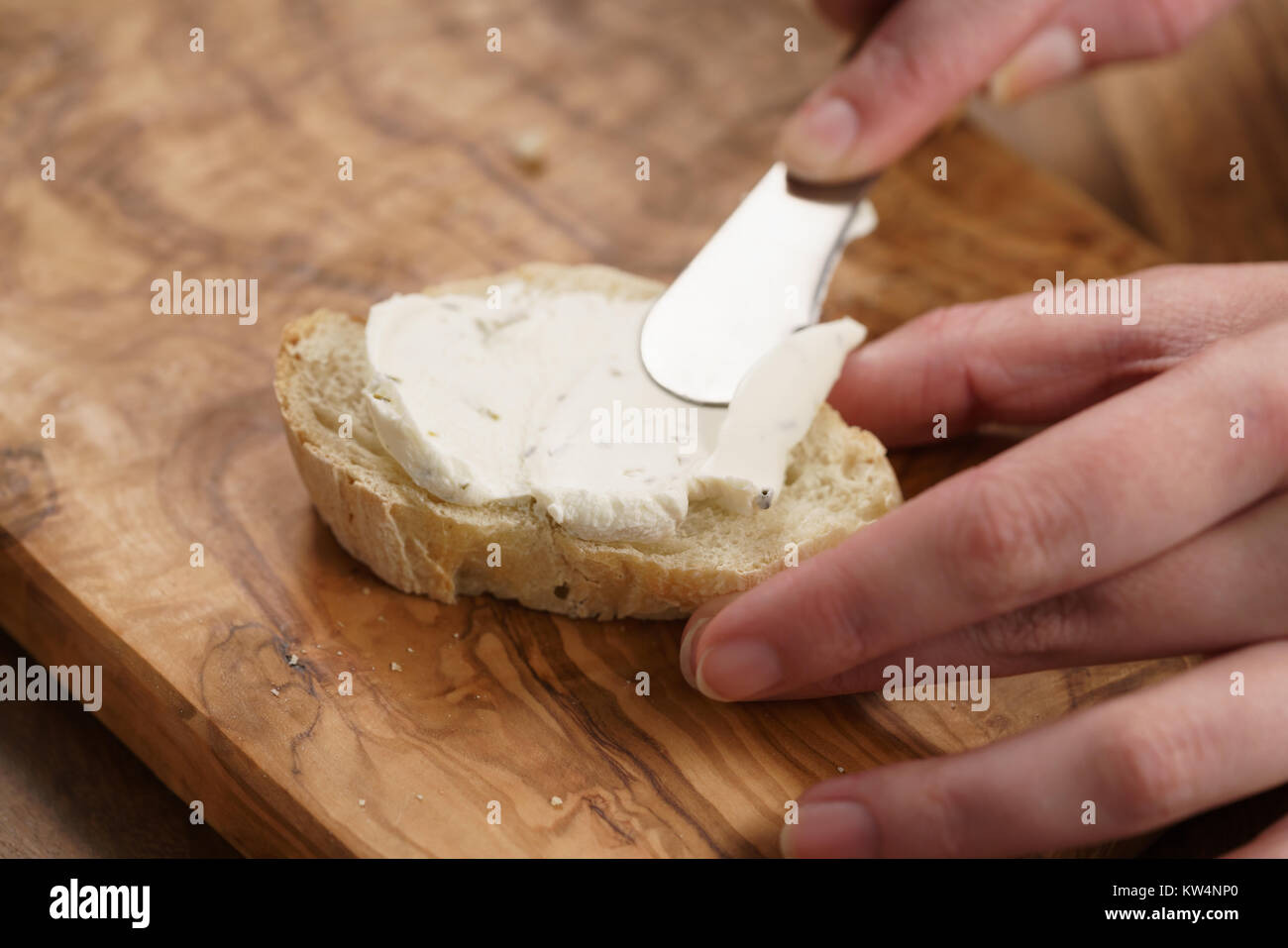 Giovani mani femminili diffondere la crema di formaggio su baguette, primo piano Foto Stock