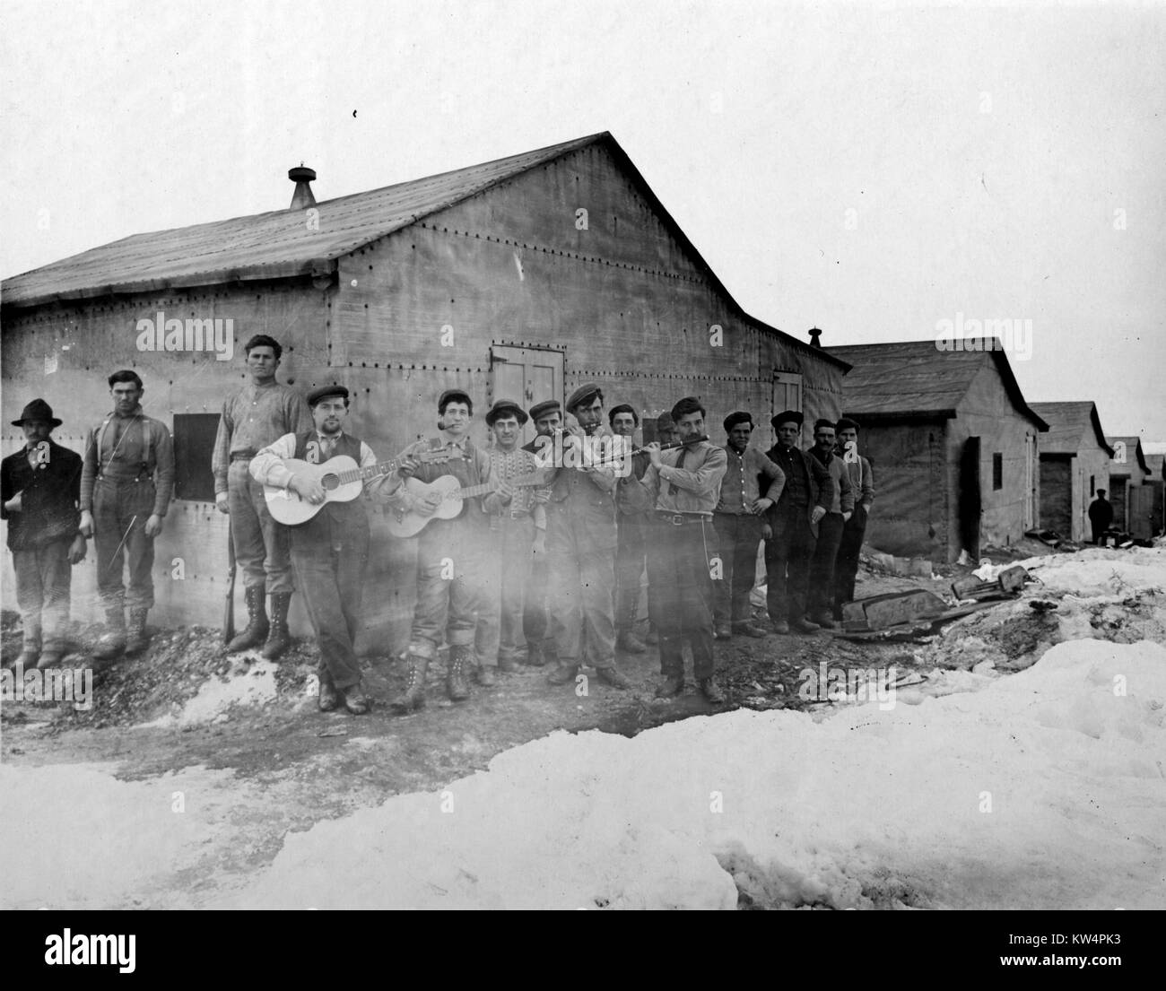 Un gruppo di lavoratori acquedotto, molti dei quali sono a suonare strumenti, sono raccolte al di fuori di una casa a castello su un accampamento durante la costruzione di un acquedotto di Catskill, New York, Stati Uniti, gennaio 20, 1910. Dalla Biblioteca Pubblica di New York. Foto Stock
