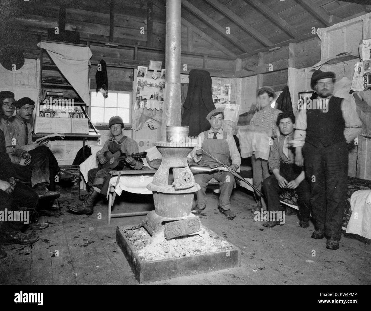 I lavoratori sono riuniti attorno a una stufa all'interno di una casa a castello su un accampamento durante la costruzione di un acquedotto di Catskill, New York, Stati Uniti, gennaio 20, 1910. Dalla Biblioteca Pubblica di New York. Foto Stock