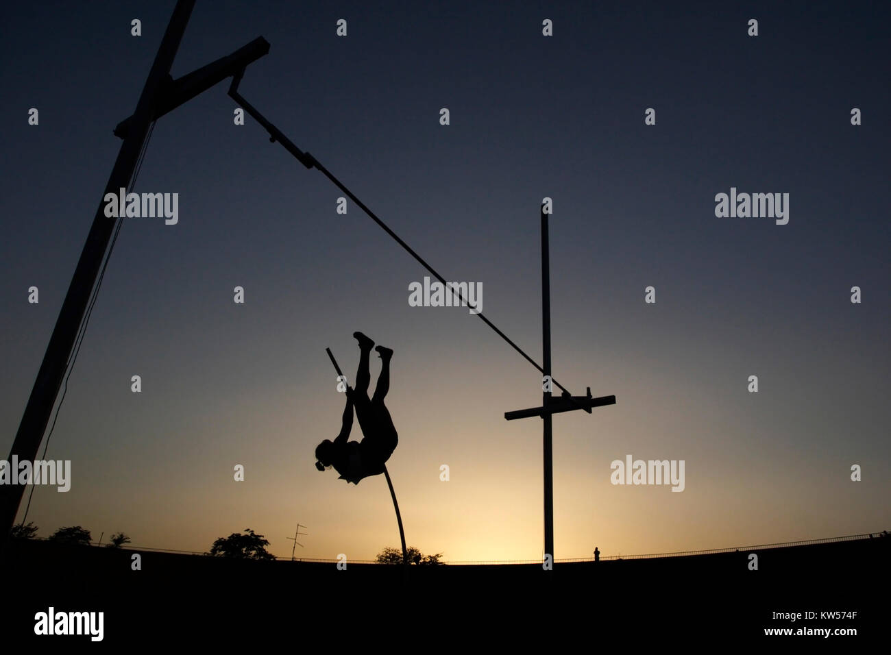Atleta competere in pole vault durante il tramonto Foto Stock