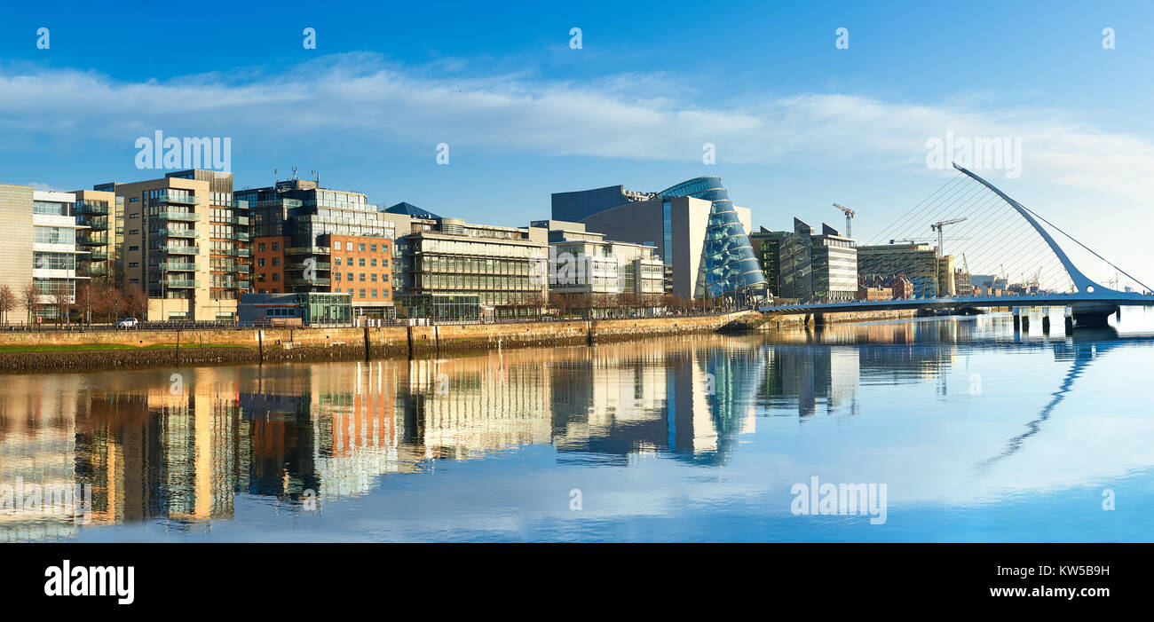 Edifici moderni e uffici sul fiume Liffey a Dublino su una luminosa giornata di sole, ponte a destra è un famoso ponte arpa. Foto Stock