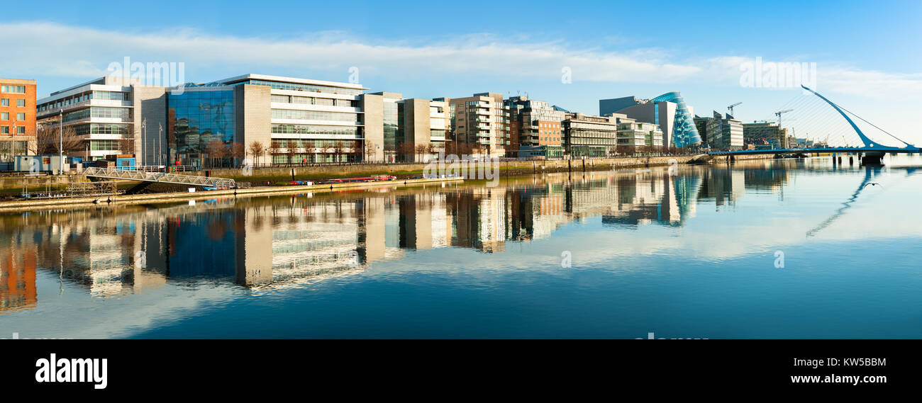 Edifici moderni e uffici sul fiume Liffey a Dublino su una luminosa giornata di sole, ponte a destra è un famoso ponte arpa. Immagine panoramica. Foto Stock