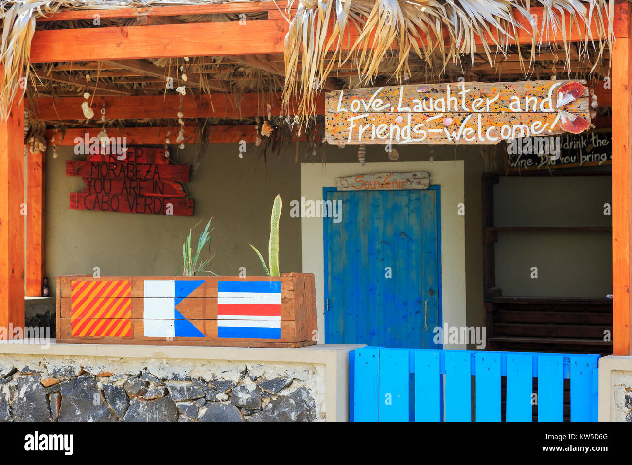 La Street View di un locale bar e negozio di souvenir con bandiere dipinte e motto appeso sulla segnaletica, Palmeira Capo Verde Foto Stock