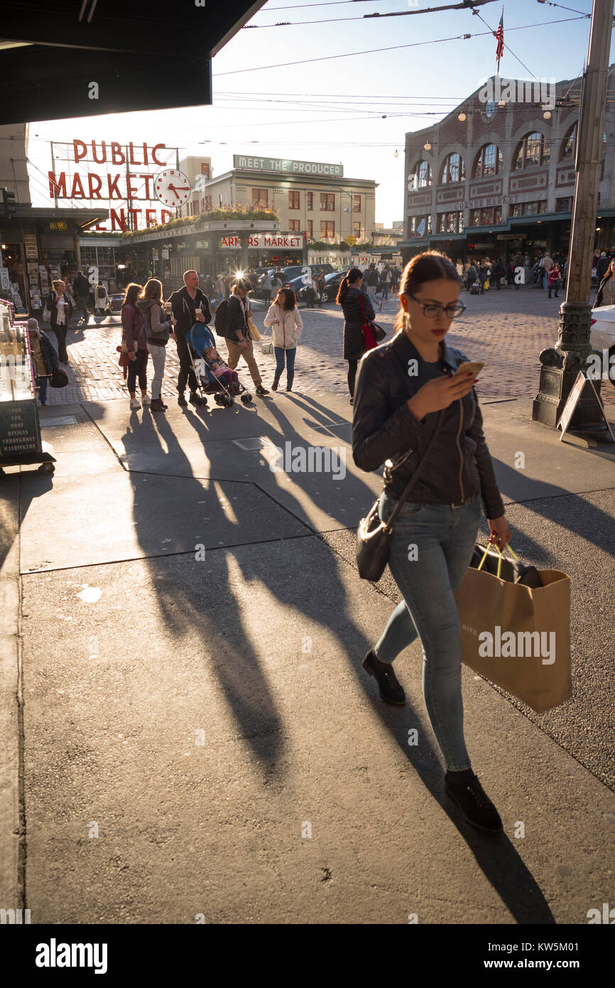 Giovane donna camminare guardando il suo telefono cellulare, il Pike Place Market, Seattle, Washington, Stati Uniti d'America Foto Stock