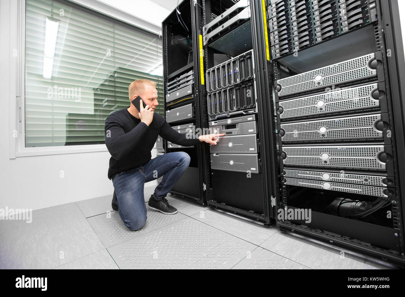 Consulente utilizza lo smartphone durante il monitoraggio dei server in Datacent Foto Stock