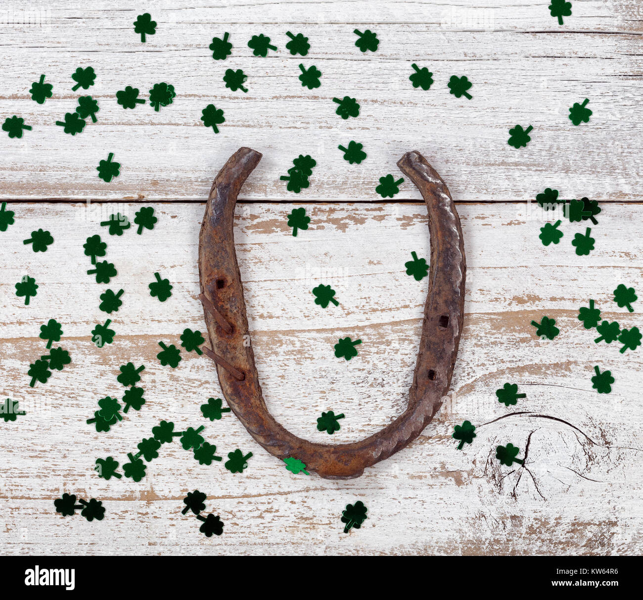 Vista ravvicinata di un ferro di cavallo arrugginito per St Patrick day con trifogli lucido su bianco a spiovente di tavole di legno Foto Stock