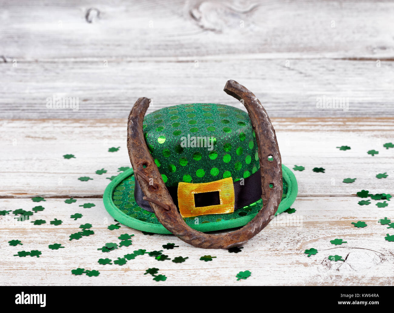 Vista ravvicinata di un ferro di cavallo arrugginito in appoggio sul cappello per St Patrick day con trifogli lucido su bianco a spiovente di tavole di legno Foto Stock