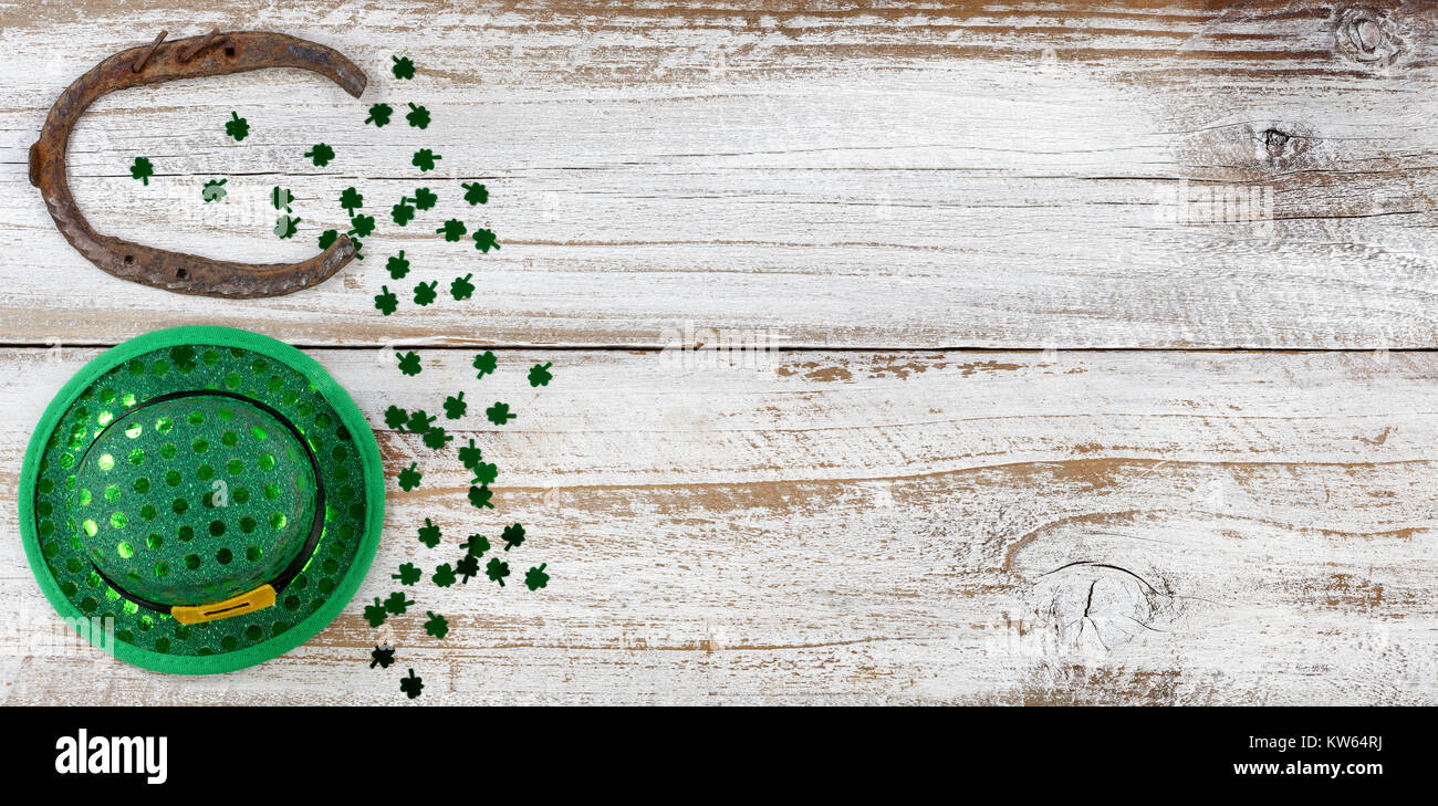 Il giorno di San Patrizio buona fortuna hat e a ferro di cavallo con scintillante trifogli formando bordo sul lato sinistro del bianco rustico di tavole di legno Foto Stock