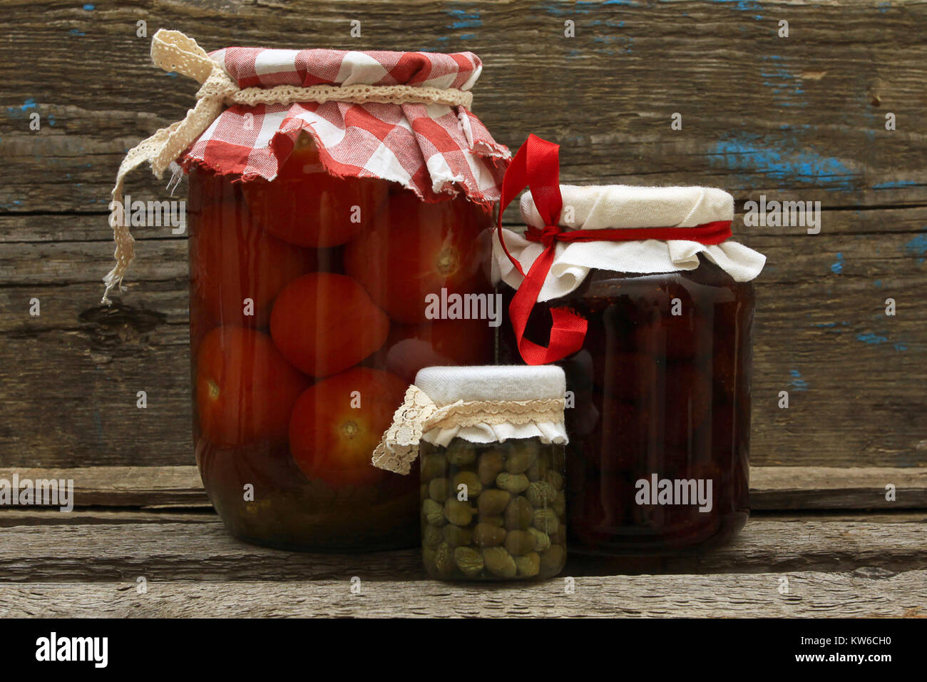 Conservare. Vaso con confettura di fragole, pomodori sott'aceto e capperi su sfondo di legno Foto Stock