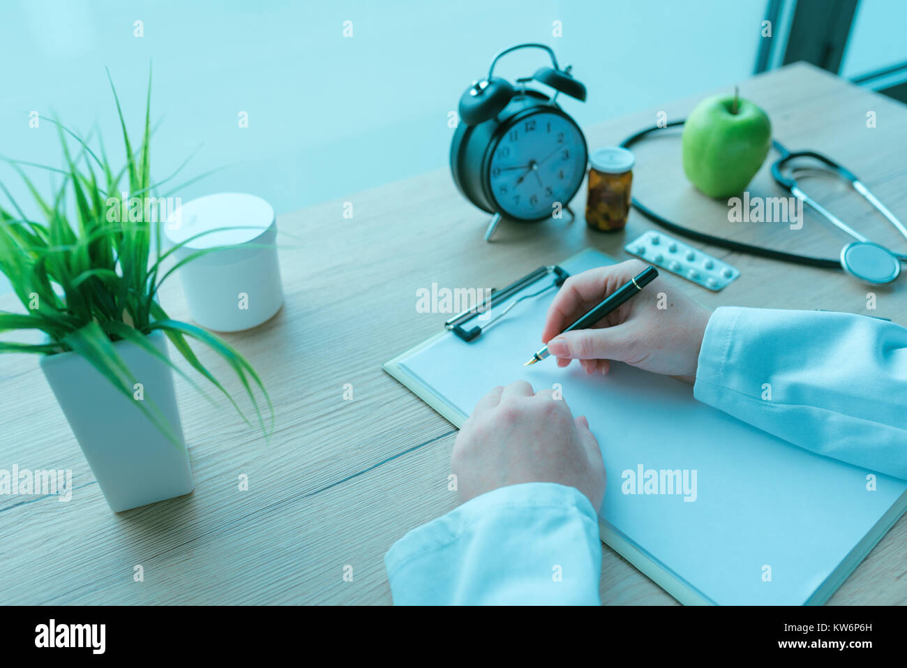Medico di medicina generale scrivere appunti durante la visita medica, la prescrizione medicina e sanità, nei toni del blu immagine Foto Stock