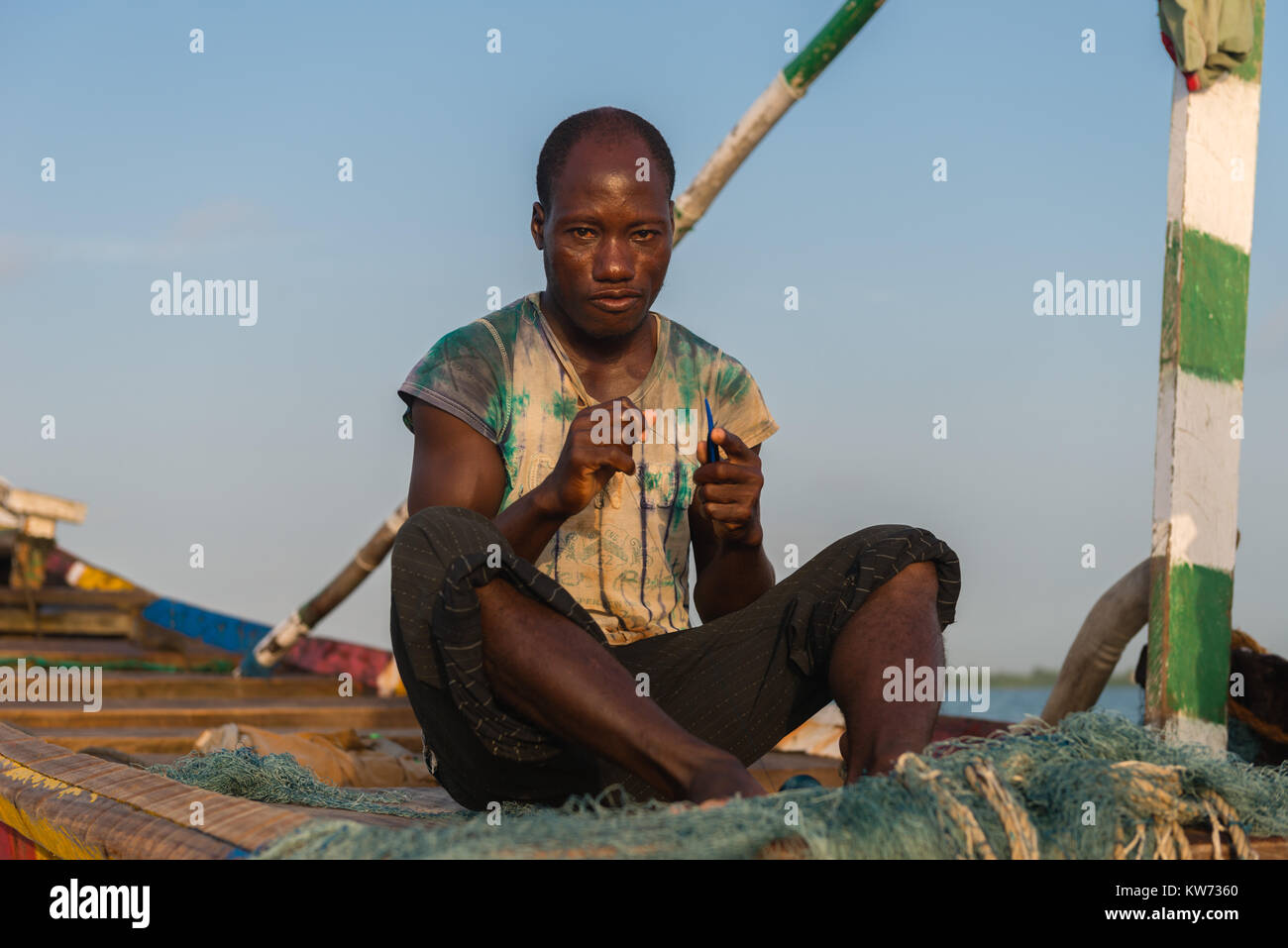 Fisherman riparare reti, seduto nella sua barca open, Volta River, Ada Foah, maggiore Regione di Accra, Ghana, Africa Foto Stock