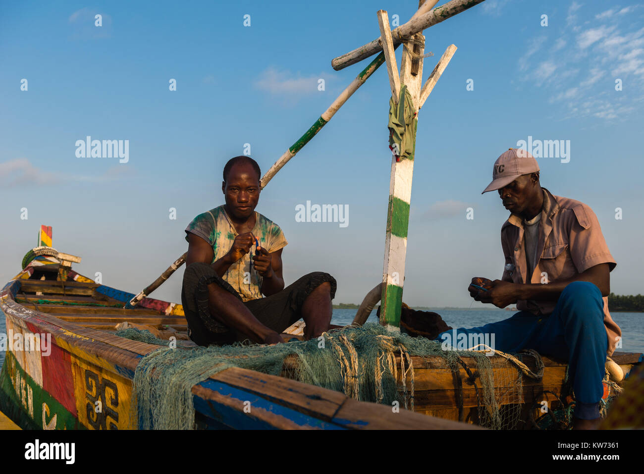 Fisherman riparare reti, seduto nella sua barca open, Volta River, Ada Foah, maggiore Regione di Accra, Ghana, Africa Foto Stock