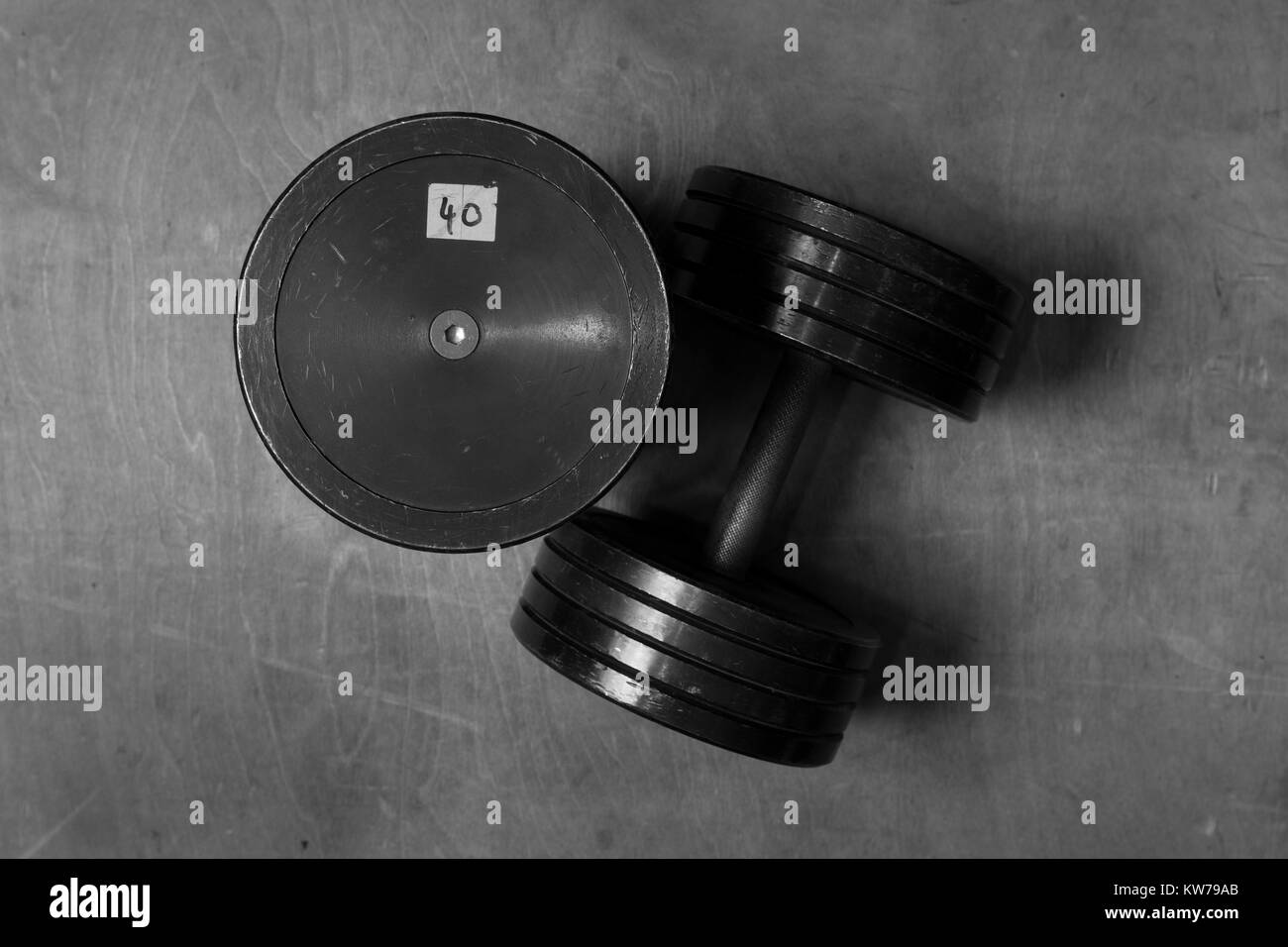 Immagine in bianco e nero di due vecchi e usato il nero pesi su un pavimento di legno in una palestra. Foto Stock