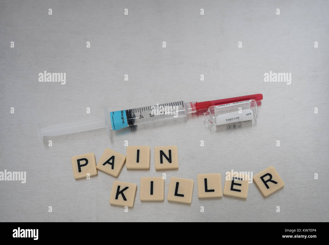 Pain Killer scritto con lettere di piastrelle collocato in un casuale con una siringa riempita con liquido chiaro e un bicchiere vuoto fentanil flaconcino. Foto Stock
