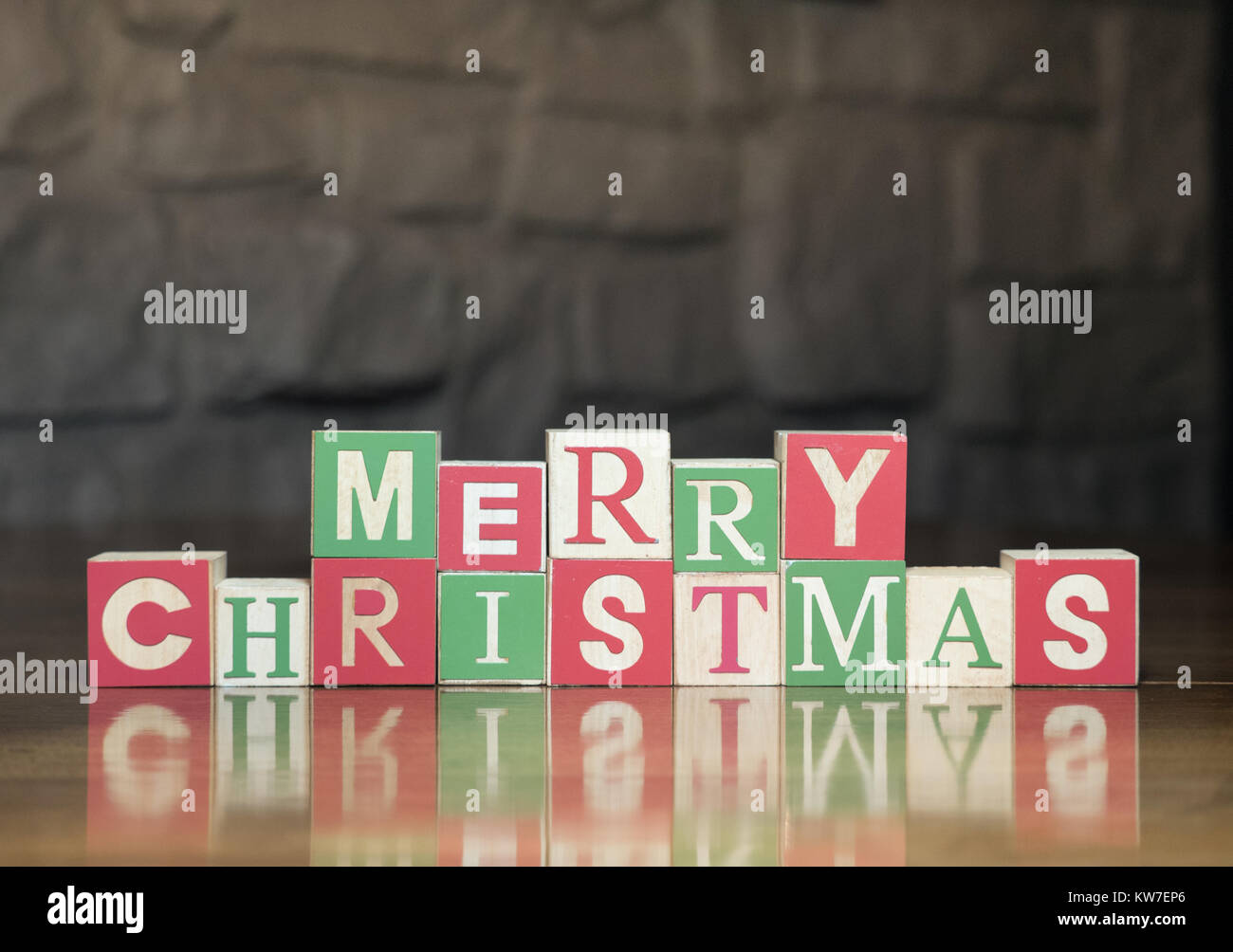 I blocchi di legno in verde, rosso e legno chiaro con lettere maiuscole ortografia Buon Natale. Fotografato con una profondità di campo ridotta su un lucido scheda di legno Foto Stock