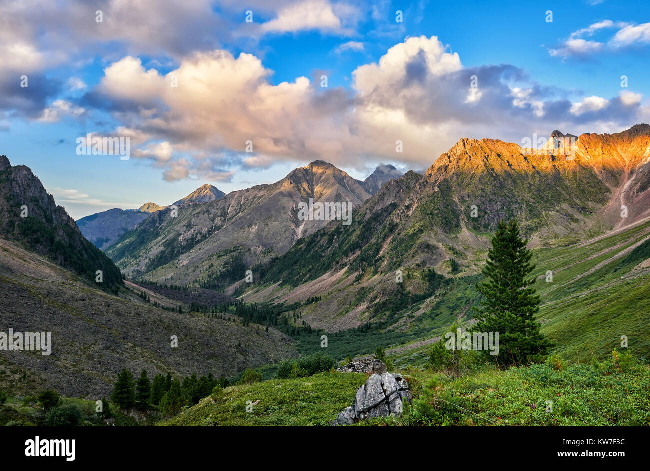 Valle di montagna in serata. Ultimi raggi di sole cadono su cumuli di nuvole e la sommità del rilievo in primo piano. Eastern Sayan. La Russia Foto Stock