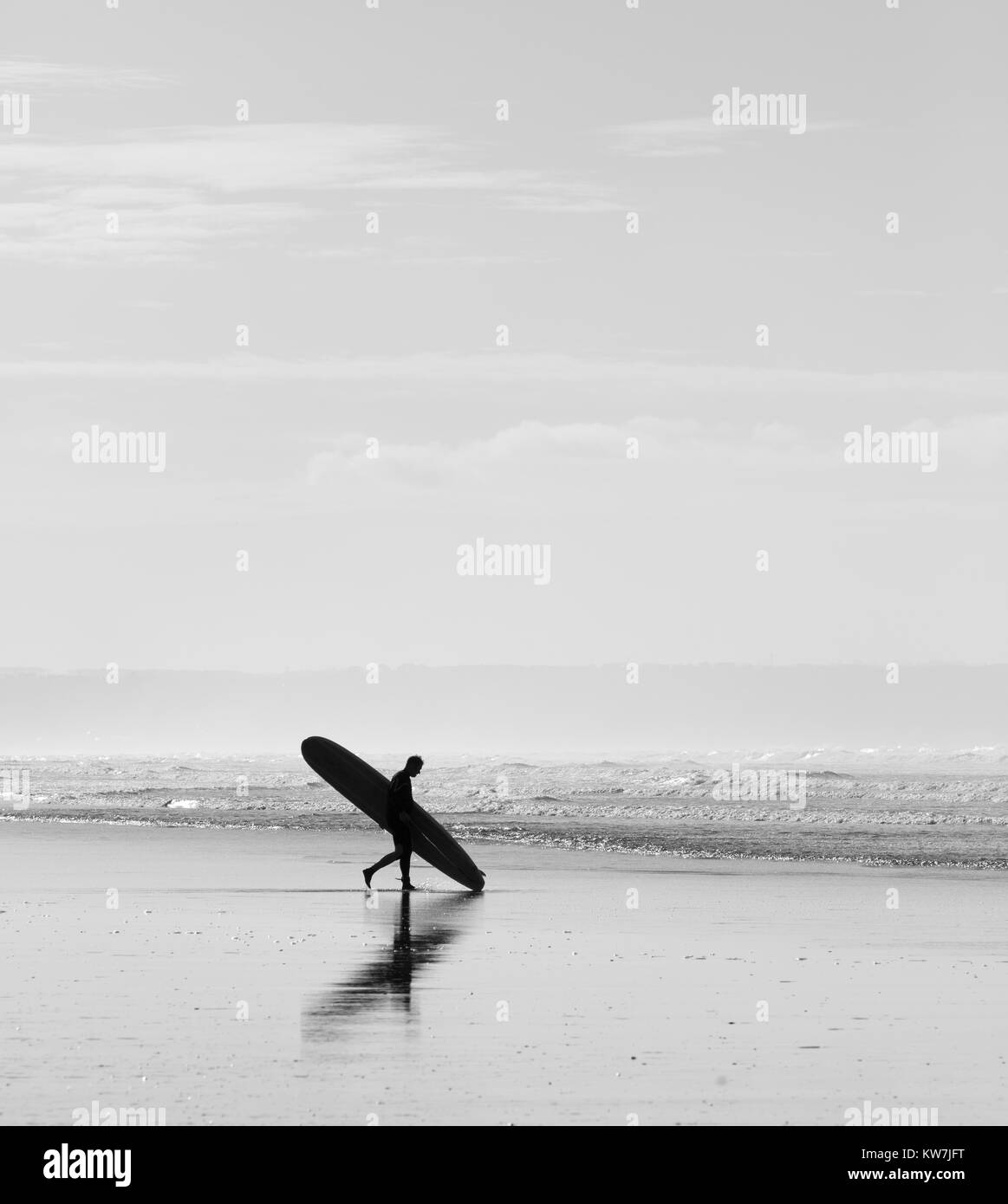 Surfer passeggiate su una spiaggia di sabbia in possesso di una tavola da surf Foto Stock
