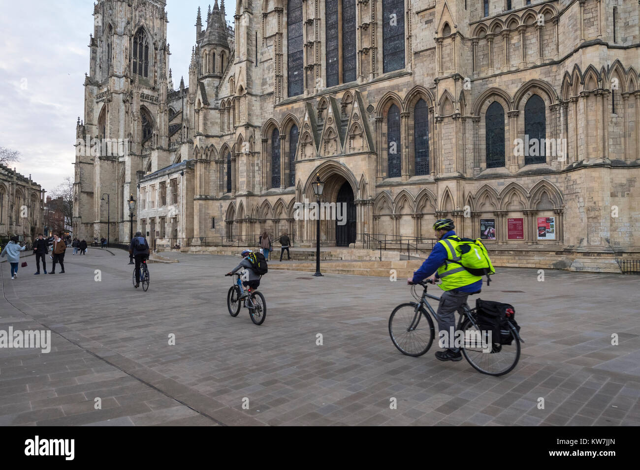 York centre - 2 adulti & 1 bambini equitazione biciclette, ciclo attraverso piazza, passato ingresso sud alla magnifica cattedrale di York Minster - North Yorkshire, Inghilterra, Regno Unito. Foto Stock