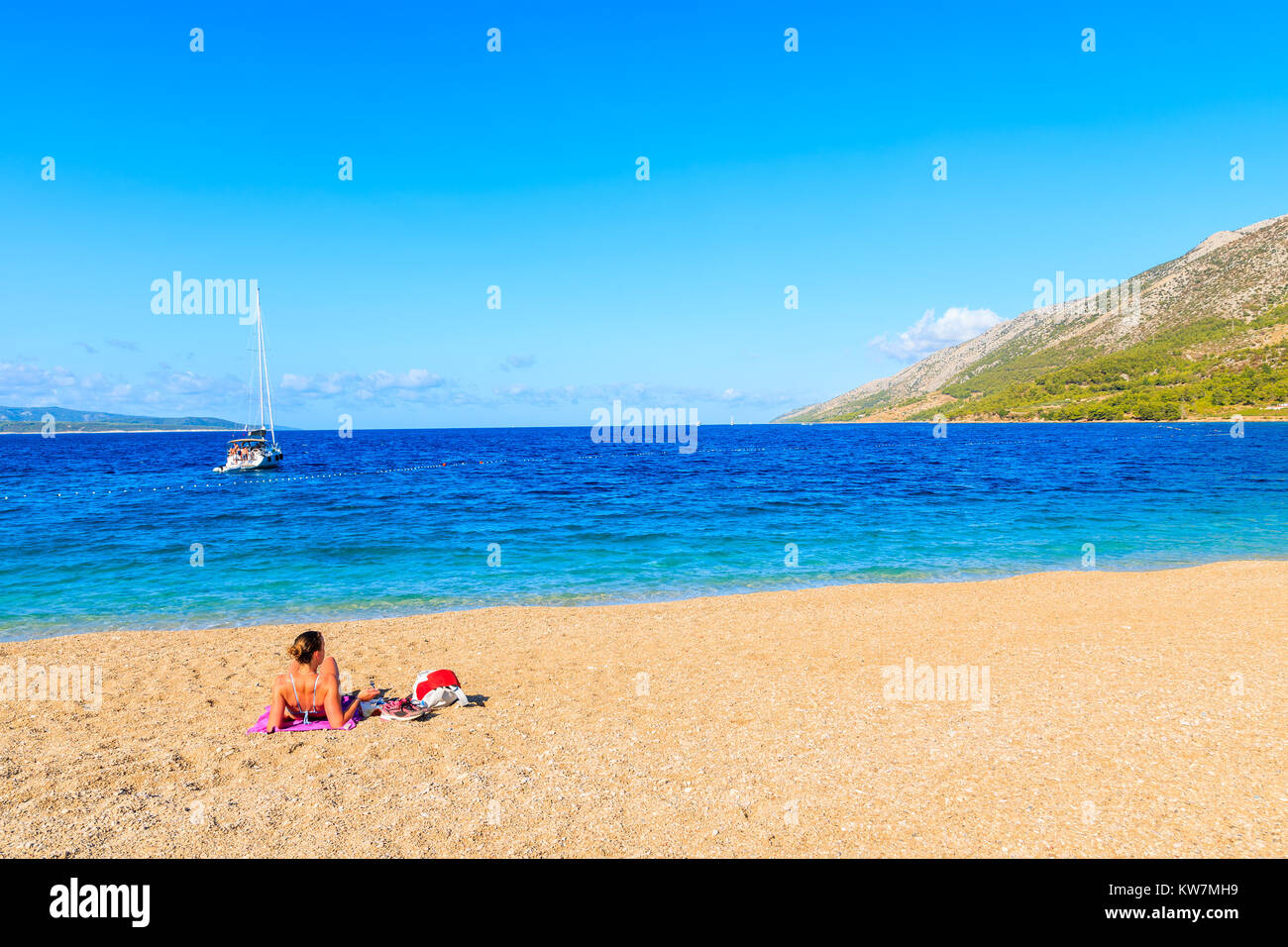 Giovane donna non identificato tourist a prendere il sole sulla spiaggia Zlatni Rat (Golden Horn) con bellissima acqua di mare, la spiaggia più famosa del Mare Adriatico, l'isola di Brac Foto Stock