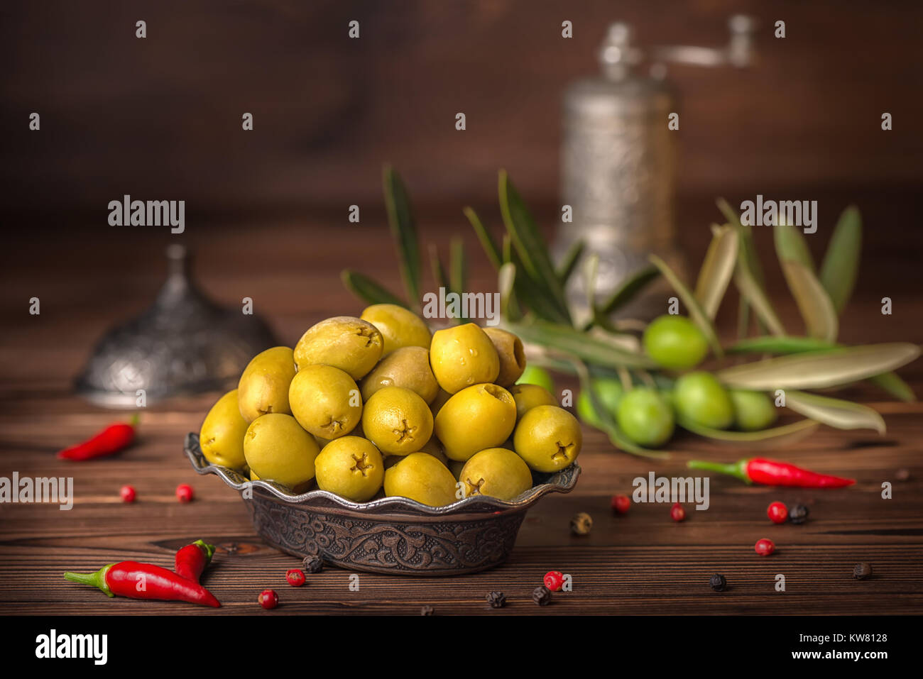 Salate olive verdi nella piastra giacciono sullo sfondo di legno decorate il peperoncino, il ramo di olivo e macinino, in stile arabo Foto Stock