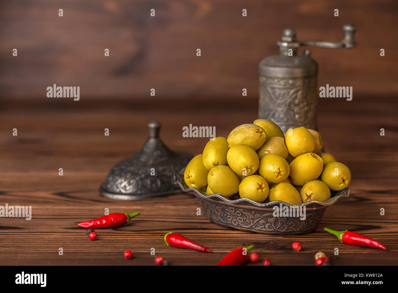 Decapare le olive verdi nella piastra giacciono sullo sfondo di legno decorate il peperoncino e la mola, in stile arabo Foto Stock