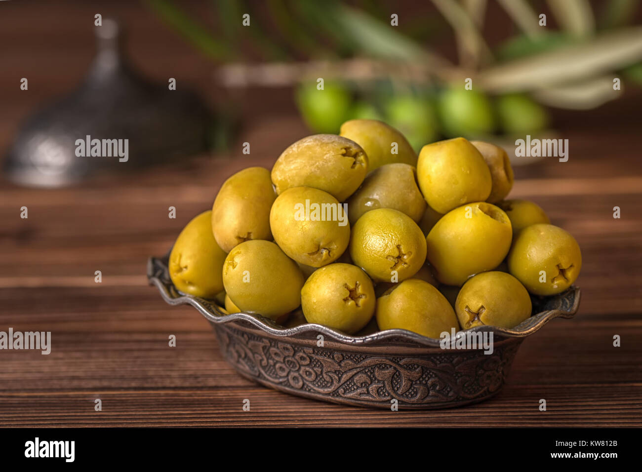 Decapare le olive verdi nella piastra giacciono sullo sfondo di legno decorate ramo di olivo e macinino, in stile arabo Foto Stock